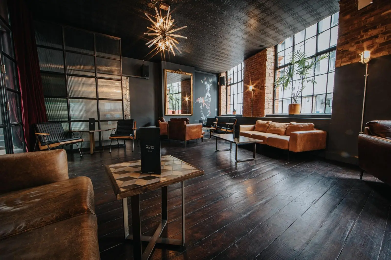 A BRIX lounge space — leather sofas, a starburst chandelier, exposed brick and tall warehouse windows