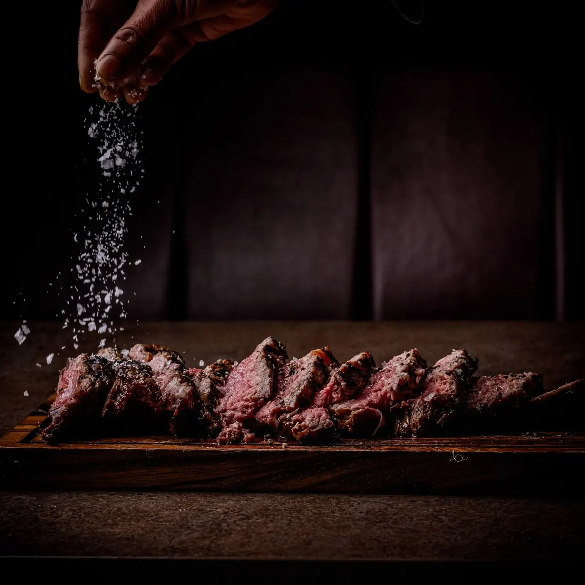 Sliced flame-grilled steak being finished with sea salt flakes