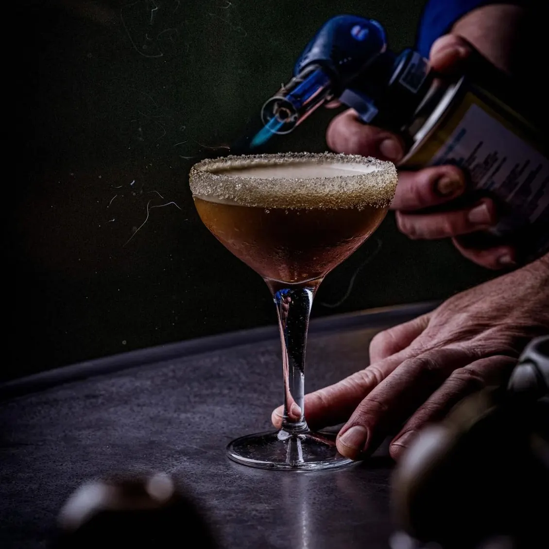 A bartender torching the sugar rim of a cocktail at SIXT33N