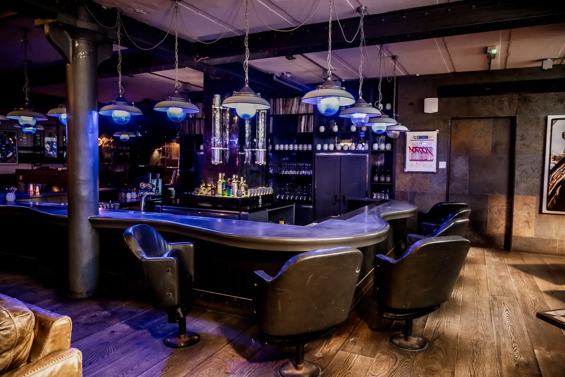 The curved bar with leather swivel seats under blue pendant lights